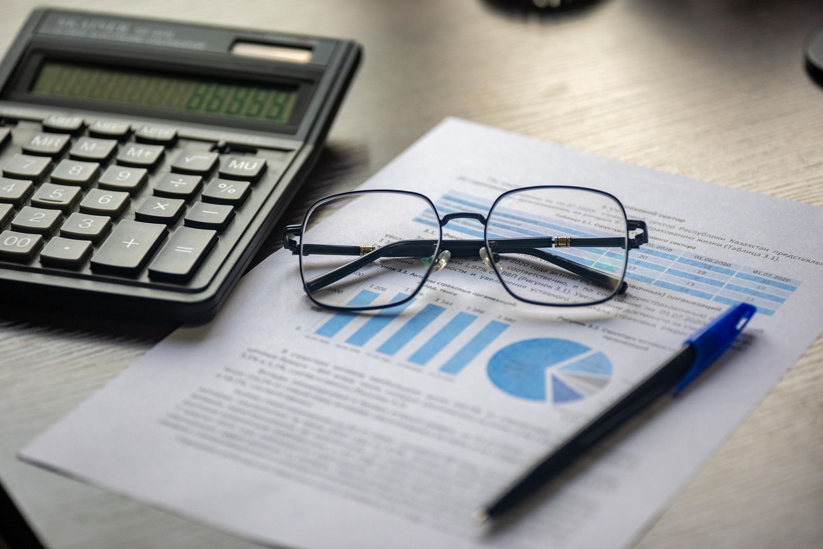 A calculator, reading glasses and a pen resting on a printed financial statement